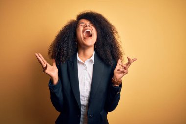 Young beautiful african american business woman with afro hair wearing elegant jacket celebrating mad and crazy for success with arms raised and closed eyes screaming excited. Winner concept clipart