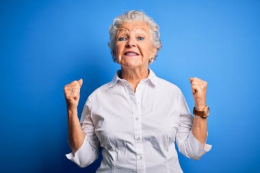 Soyutlanmış mavi arka plan üzerinde duran zarif gömlek giyen son sınıf güzeli kadın kollarını kaldırarak ve açık gözlerle başarının şaşkınlığını ve hayretini yaşıyor. Kazanan konsept.