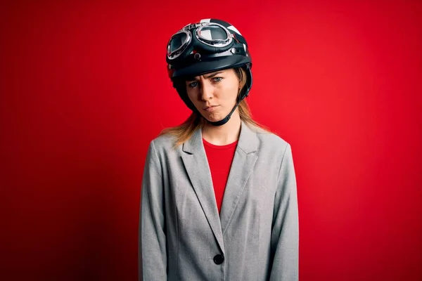 若い美しいブロンドのオートバイの女性は 問題のために動揺を眉をひそめて 赤い背景懐疑的かつ神経の上にオートバイのヘルメットをかぶっている 負の人 — ストック写真