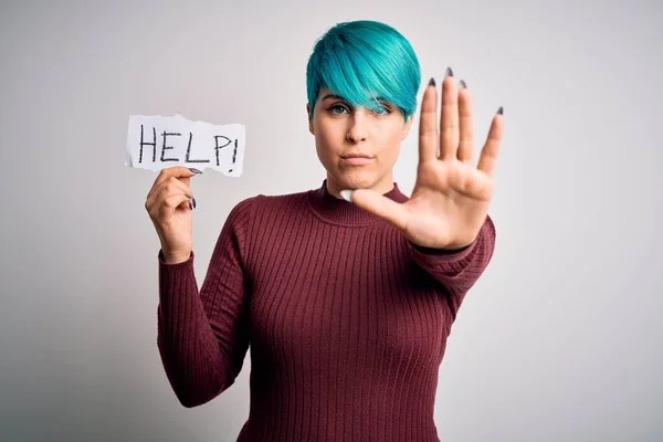 Young woman with blue fashion hair asking for help showing message on paper with open hand doing stop sign with serious and confident expression, defense gesture