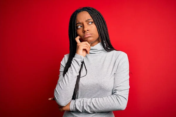 若いアフリカ系アメリカ人の女性は 赤い隔離された背景にタートルネックのセーターを着ており 顎は質問 集中的な表現について考えています 思慮深い顔で微笑んだ 疑いの概念 — ストック写真