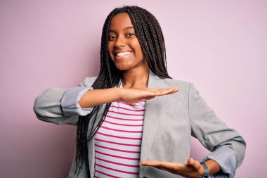 Genç Afrikalı Amerikalı iş kadını pembe izole edilmiş arka planda duruyor. Ellerinde büyük ve büyük boy işareti, ölçü sembolü var. Kameraya bakıp gülümsüyor. Ölçüm konsepti.