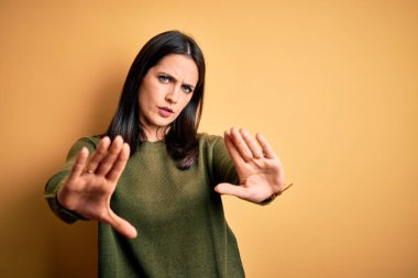 Sarı arka planda yeşil süveter giyen, mavi gözlü genç esmer kadın avuç içi hareketlerini durduruyor, kızgın ve hayal kırıklığına uğramış yüz ifadesi takınıyor.