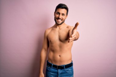 Genç, yakışıklı, sakalsız, pembe arka planda duran yakışıklı, güçlü bir adam. Dostça bir selamlama ve hoş geldin hediyesi olarak gülümsüyor. Başarılı bir iş..