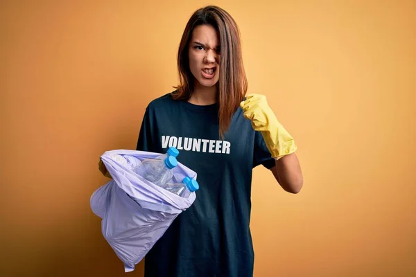 Beautiful volunteer girl caring environment doing volunteering holding bag with rubish bottles annoyed and frustrated shouting with anger, crazy and yelling with raised hand, anger concept