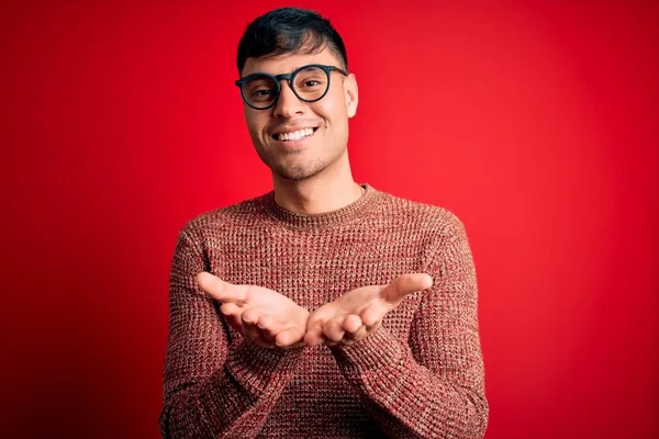 Mladý Pohledný Hispánec Šprtských Brýlích Červeném Pozadí Usmívá Dlaněmi Přijímá — Stock fotografie