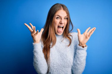 Genç, güzel, kızıl saçlı bir kadın mavi arka plan üzerine günlük süveter giyip çılgın ve başarıyı kollarını kaldırıp heyecanla haykırarak kutluyor. Kazanan konsept