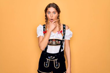 Geleneksel Ekim Festivali elbisesi giyen, mavi gözlü, genç, güzel, sarışın bir Alman kadın. İnançsızlıktan, şaşkınlıktan ve hayrete düşmüş, elleri çenesinde olan bir ifadeyle.