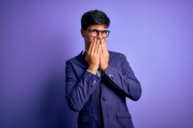 Ceket ve gözlük takan genç yakışıklı iş adamı mor arka planda gülüyor ve utanıyor kıkırdıyor ağzı ellerle, dedikoduyla ve skandal konseptiyle örtüyor.