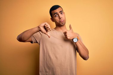 Genç, yakışıklı, Afro-Amerikalı bir adam sarı arka planda dikilen günlük tişörtler giyiyor. Baş parmaklarını kaldırıyor, anlaşmazlık ve uzlaşma ifadesi sergiliyor. Çılgın çatışma