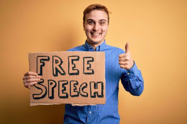 Genç, yakışıklı, kızıl saçlı, özgürlük isteyen özgür konuşma mesajıyla bayrak tutan mutlu ve pozitif gülümseyen, mükemmel ve onay işareti yapan bir adam.