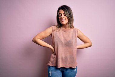 Moda kıyafetleri giyen genç ve güzel bir kadın. Manken, sokak tarzı giyiniyor. Pembe arka planda dikiliyor.