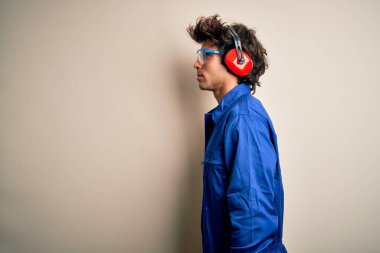 Üniforma giyen ve kulaklık takan genç müteahhit beyaz arka plana bakıyor, rahat profil pozu veriyor, kendine güveni tam bir gülümseme takınıyor..