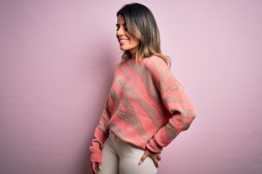 Moda kıyafetleri giyen genç ve güzel bir kadın. Manken, sokak tarzı giyiniyor. Pembe arka planda dikiliyor.