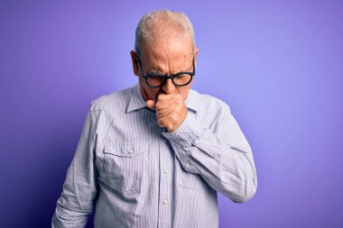 Mor arka planda çizgili gömlek ve gözlük takan orta yaşlı yakışıklı adam kendini kötü hissediyor ve soğuk algınlığı veya bronşitin belirtisi olarak öksürüyor. Sağlık hizmeti kavramı.