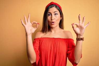 Sarıya boyanmış arka plan üzerinde renkli genç bir kadın. Şaşırmış ve şaşırmış görünüyor. Parmaklarıyla onay sembolü yapıyor. Çılgın ifade