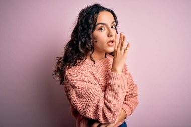 Kıvırcık saçlı, günlük süveter giyen, pembe arka planı olan genç ve güzel bir kadın. Ağzında gizli dedikodular dolaşıyor, kötü niyetli konuşmalar fısıldıyor.