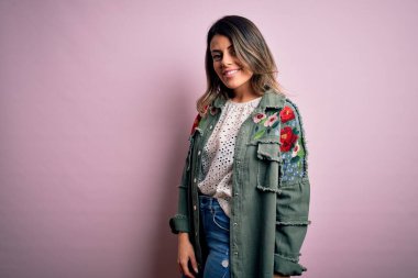 Moda kıyafetleri giyen genç ve güzel bir kadın. Manken, sokak tarzı giyiniyor. Pembe arka planda dikiliyor.