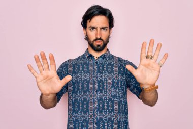 Pembe arka planda hippi tarzı giyinmiş genç, Latin asıllı bohem adam avuç içi hareketlerini durduruyor, kızgın ve hayal kırıklığına uğramış yüz ifadesi takınıyor.