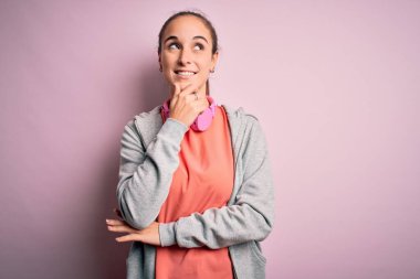 Spor yapan güzel bir kadın müzik dinliyor pembe arka planda kulaklık takıyor, elleri çenesinde soru soruyor, düşünceli bir yüz ifadesi var. Düşünceli bir yüzle gülümsüyor. Şüphe kavramı.