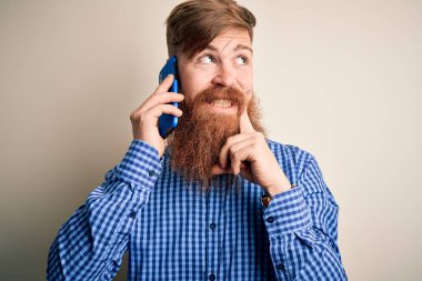 Kızıl saçlı, sakallı bir İrlandalı, akıllı telefondan konuşuyor. Tecrit edilmiş bir arka planda. Ciddi bir yüz.