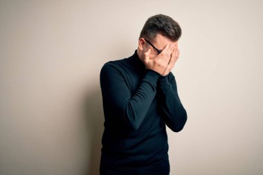 Gözlük takan yakışıklı beyaz bir adam ve izole edilmiş arka planda sıradan bir süveter giyiyor. Ağlarken yüzünü ellerle kapatan üzgün bir yüz ifadesi var. Depresyon kavramı.