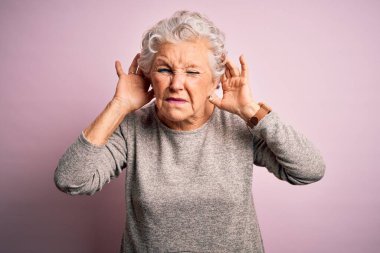 Üst düzey güzel bir kadın pembe arka plan üzerinde günlük tişört giyip iki elini de kulak hareketi yaparken duymaya çalışıyor. Dedikoduya meraklı. İşitme problemi, sağır