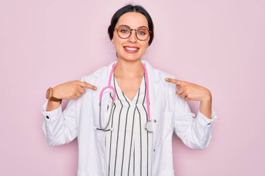 Pembe arka planda mavi gözlü ve steteskop takmış güzel bir doktor. Yüzünde bir gülümsemeyle, gururlu ve mutlu parmaklarıyla kendini işaret ediyor..