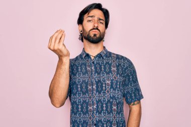 Pembe arka planda hippi tarzı giyinmiş genç, Latin asıllı bohem bir adam İtalyanca jestler yapıyor.