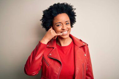 Young beautiful African American afro woman with curly hair wearing casual red jacket smiling doing phone gesture with hand and fingers like talking on the telephone. Communicating concepts.