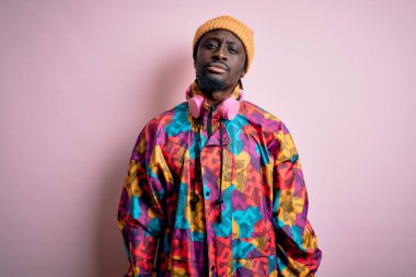 Pembe arka plan üzerine renkli palto ve şapka giyen yakışıklı Afro-Amerikan bir adam. Yüzünde ciddi bir ifadeyle rahatlamış. Basit ve doğal bir şekilde kameraya bakıyorsun..