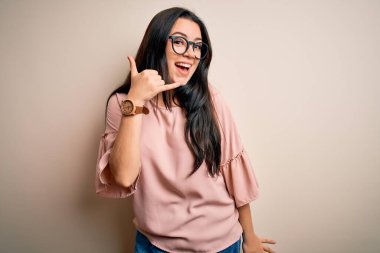 Soyutlanmış arka planda gözlük takan zarif, genç bir kadın telefonla el ve parmak hareketleriyle gülümsüyor, telefonda konuşuyor gibi. İletişim kavramları.