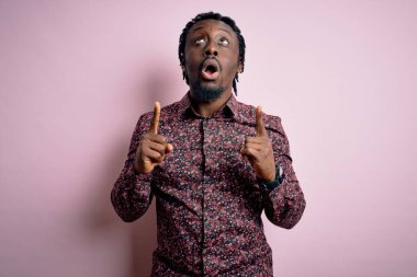 Genç, yakışıklı, Afro-Amerikalı bir adam pembe arka planda dikilmiş şaşkın şaşkın bakıyor, parmaklarıyla işaret ediyor ve kollarını kaldırıyordu..