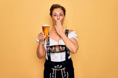 Orta yaşlı esmer kadın geleneksel Alman Ekim Festivali elbisesi giyiyor. Bir bardak bira içiyorlar. Ağızlarını kapatıyorlar.