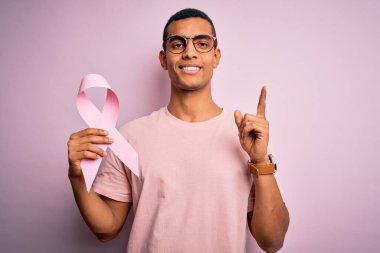 Genç, yakışıklı, Afro-Amerikan bir adam pembe kanser kurdelesini soyutlanmış arka planda saklıyor. Bir fikir ya da soruyla şaşırmış, mutlu bir yüzle işaret ediyor.