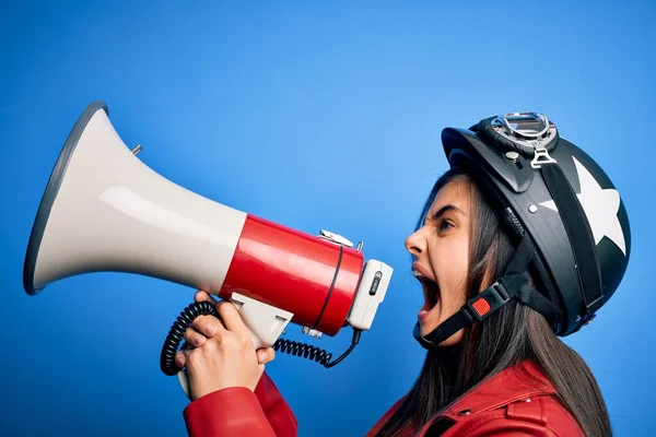 Hispanic woman wearing vintage motorbike helmet shouting angry on protest through megaphone. Yelling excited on ludspeaker talking and screaming news