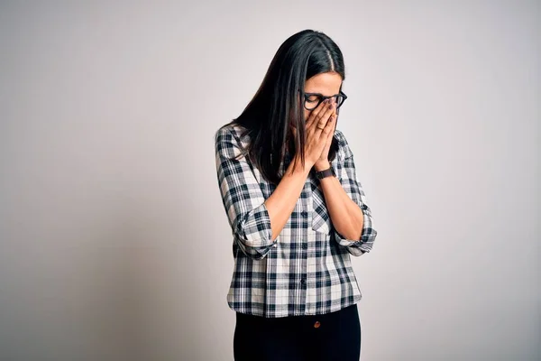 年轻的黑发女人 蓝眼睛 身穿休闲服 戴着眼镜 背景是白色的 脸上挂着忧郁的表情 哭泣的时候用手捂住脸 抑郁症的概念 — 图库照片