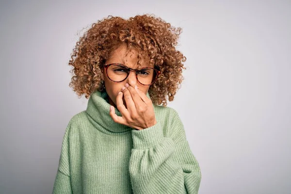 若い美しいアフリカ系アメリカ人の女性は 鼻の上に指で息を保持し 何か臭くて嫌な 耐え難い匂いを嗅ぐタートルネックセーターと眼鏡を着ています 匂いが悪い — ストック写真