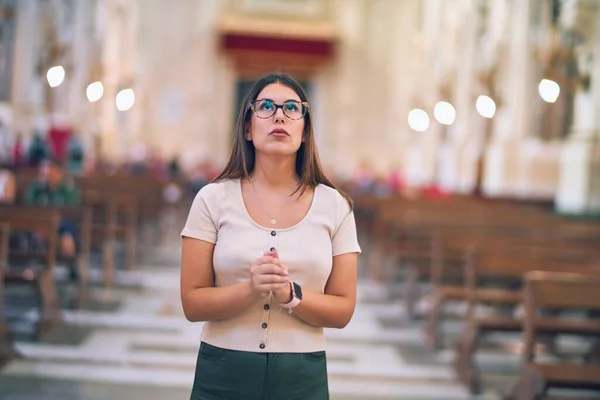 Young beautiful woman standing with hands together praying at church