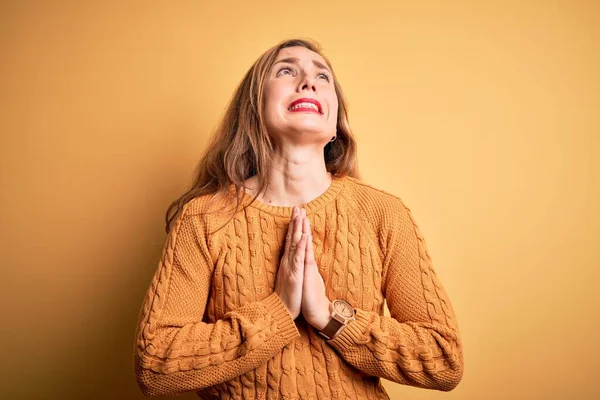 Young beautiful blonde woman wearing casual sweater standing over yellow background begging and praying with hands together with hope expression on face very emotional and worried. Begging.