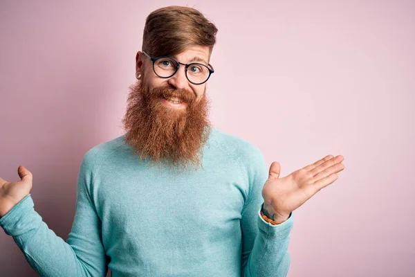 ハンサムなアイルランドの赤毛男で髭を生やして眼鏡をかけてピンク色の孤立した背景笑顔両方の手を示していますオープンヤシ プレゼンテーションと広告の比較とバランス — ストック写真