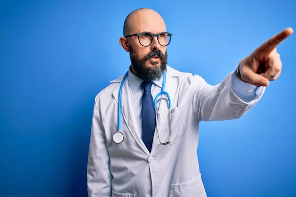Pohledný Holohlavý Lékař Vousy Brýlích Stetoskopem Modrém Pozadí Ukazující Prstem — Stock fotografie