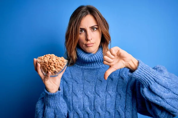 Young Beautiful Brunette Woman Holding Bowl Peanuts Blue Background Angry — Stock Photo, Image