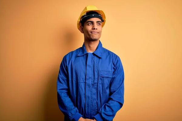 若いですハンサムなアフリカ系アメリカ人労働者の男は青い制服とセキュリティヘルメットを着て笑顔側を見て離れて考えて見つめて — ストック写真