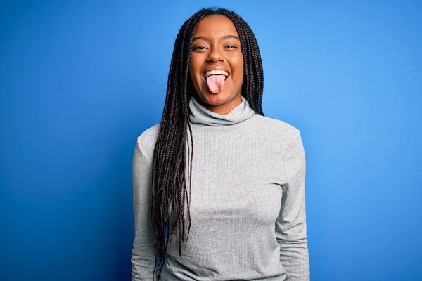 青い隔離された背景にカジュアルなタートルネックを身に着けて立っている若いアフリカ系アメリカ人女性は面白い表情で幸せ舌を突き出しています 感情概念 — ストック写真
