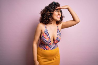 Tatilde olan güzel bir Arap kadın. Pembe arka planda mayo ve güneş gözlüğü takıyor. Çok mutlu ve gülümsüyor. Konsept aranıyor.