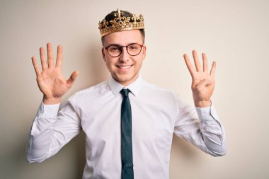 İzole edilmiş arka planda altın taç takan yakışıklı beyaz iş adamı dokuz numaralı parmaklarını gösterip gülümserken kendinden emin ve mutlu görünüyor..