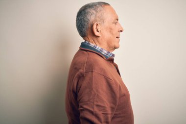 Zarif bir süveter giyen yakışıklı bir adam soyutlanmış beyaz arka planda duruyor. Yan tarafa bakıyor, rahat poz veriyor, kendine güvenen bir gülümsemesi var..