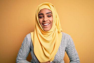 Genç ve güzel Afro-Amerikalı kız izole edilmiş sarı arka plan üzerinde Müslüman başörtüsü takıyor. Gülümsüyor ve kahkahalarla gülüyor..
