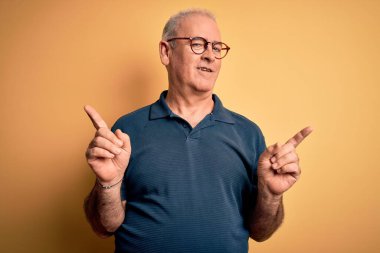 Orta yaşlı, beyaz tenli, sıradan polo giyen, sarı arka planda gözlüklü, kendine güvenen, farklı yönleri gösteren yakışıklı bir adam. Reklam için boşluk kopyala